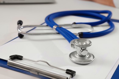 Photo of Clipboard and stethoscope on white table, closeup