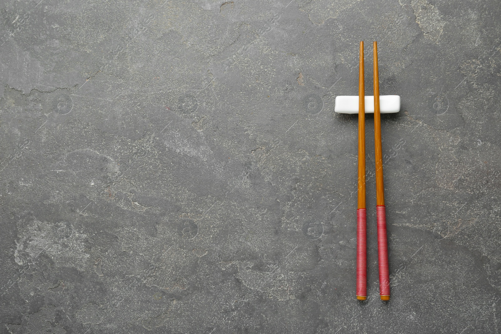 Photo of Pair of wooden chopsticks with rest on grey table, top view. Space for text