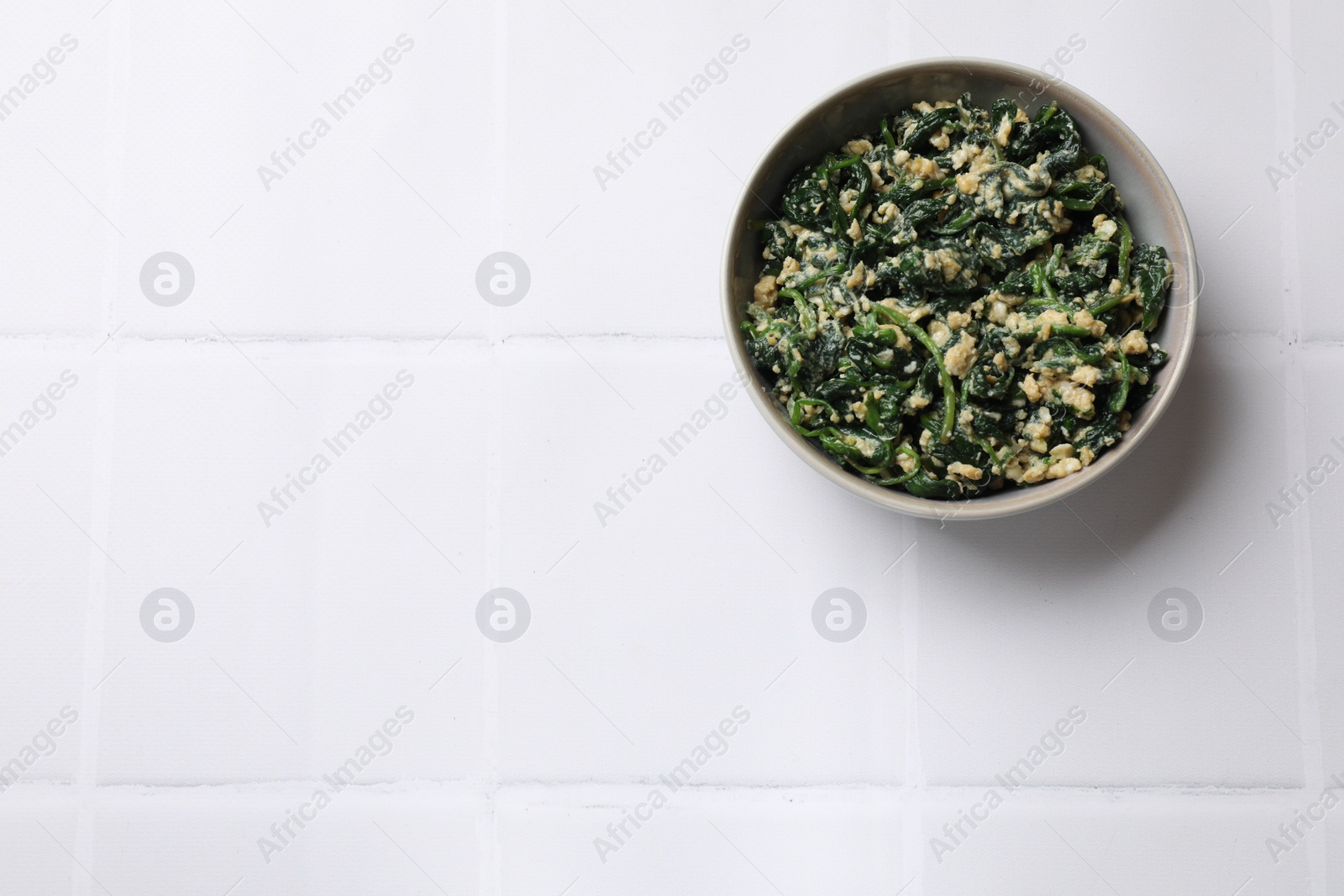 Photo of Tasty spinach dip with egg in bowl on white tiled table, top view. Space for text