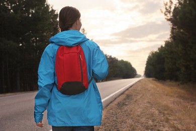 Young woman with backpack on road near forest, back view