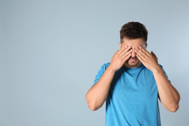 Young man being blinded on grey background, space for text