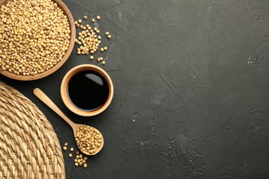 Soy sauce in bowl and soybeans on black textured table, flat lay. Space for text