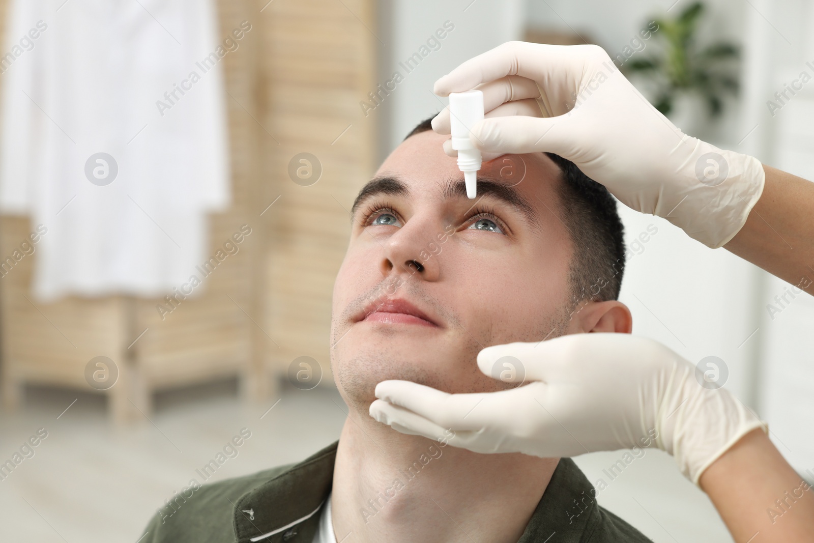 Photo of Doctor applying medical drops into young man's eye indoors