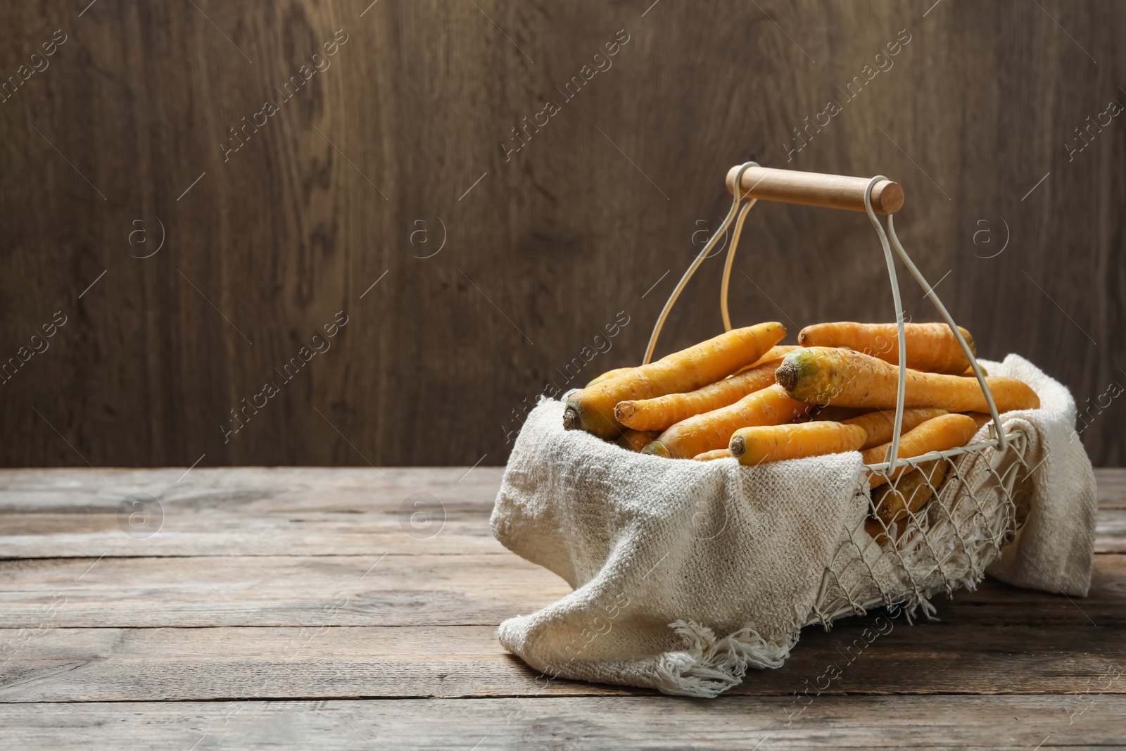 Photo of Raw yellow carrots in metal basket on wooden table. Space for text