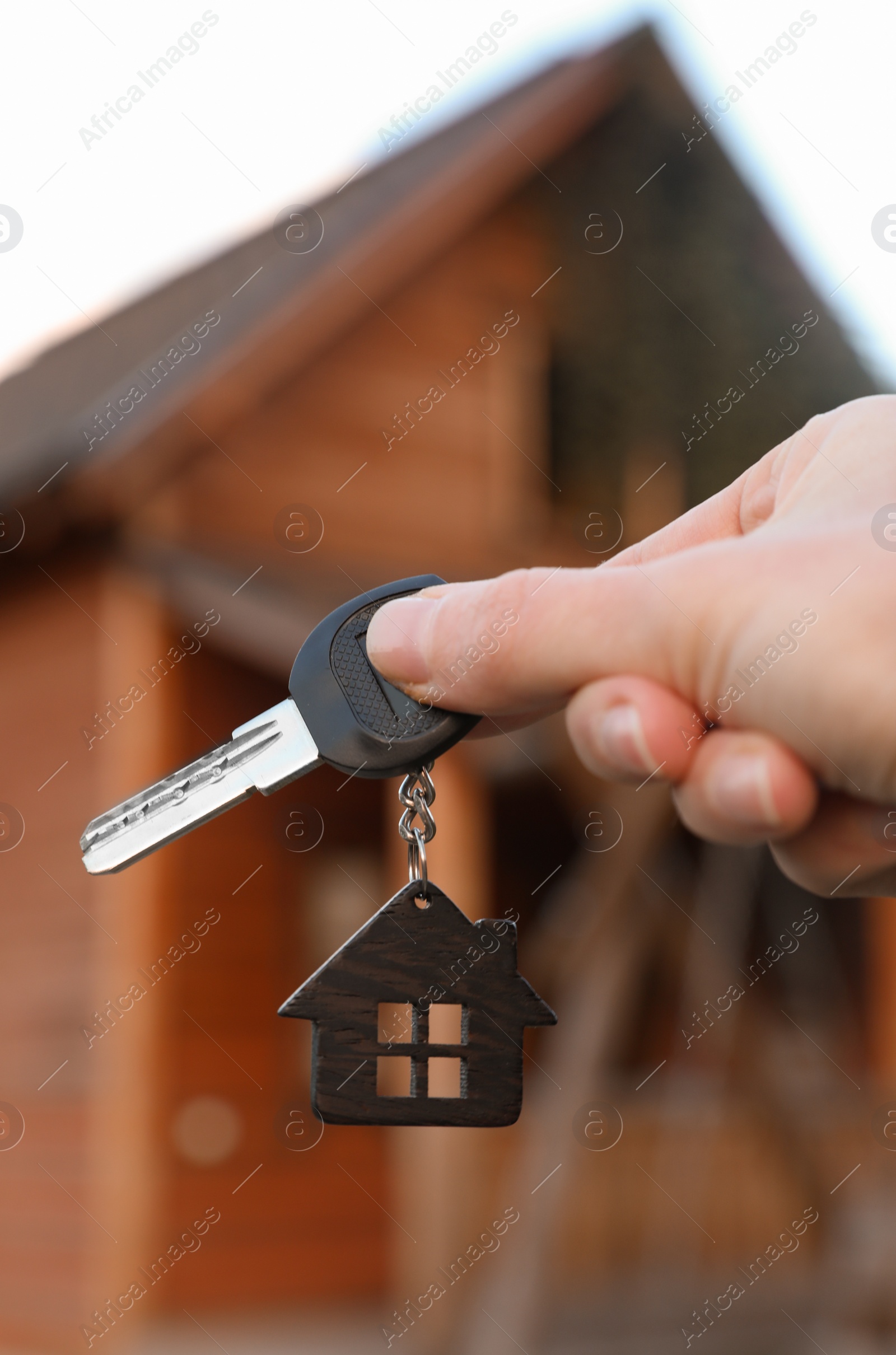 Photo of Real estate agent holding key and blurred house on background. Focus on hand