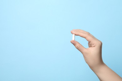 Woman holding pill on light blue background, closeup. Space for text