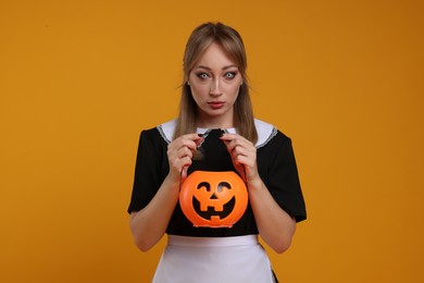Photo of Woman in scary maid costume with pumpkin bucket on orange background. Halloween celebration