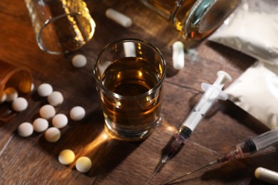 Photo of Alcohol and drug addiction. Whiskey in glass, syringes, pills and cocaine on wooden table, closeup