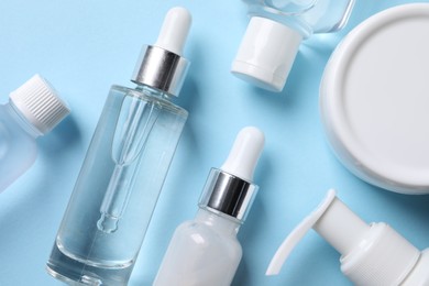 Many different bottles of cosmetic serum on light blue background, flat lay