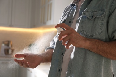 Photo of Man applying spray sanitizer onto hand in kitchen, closeup