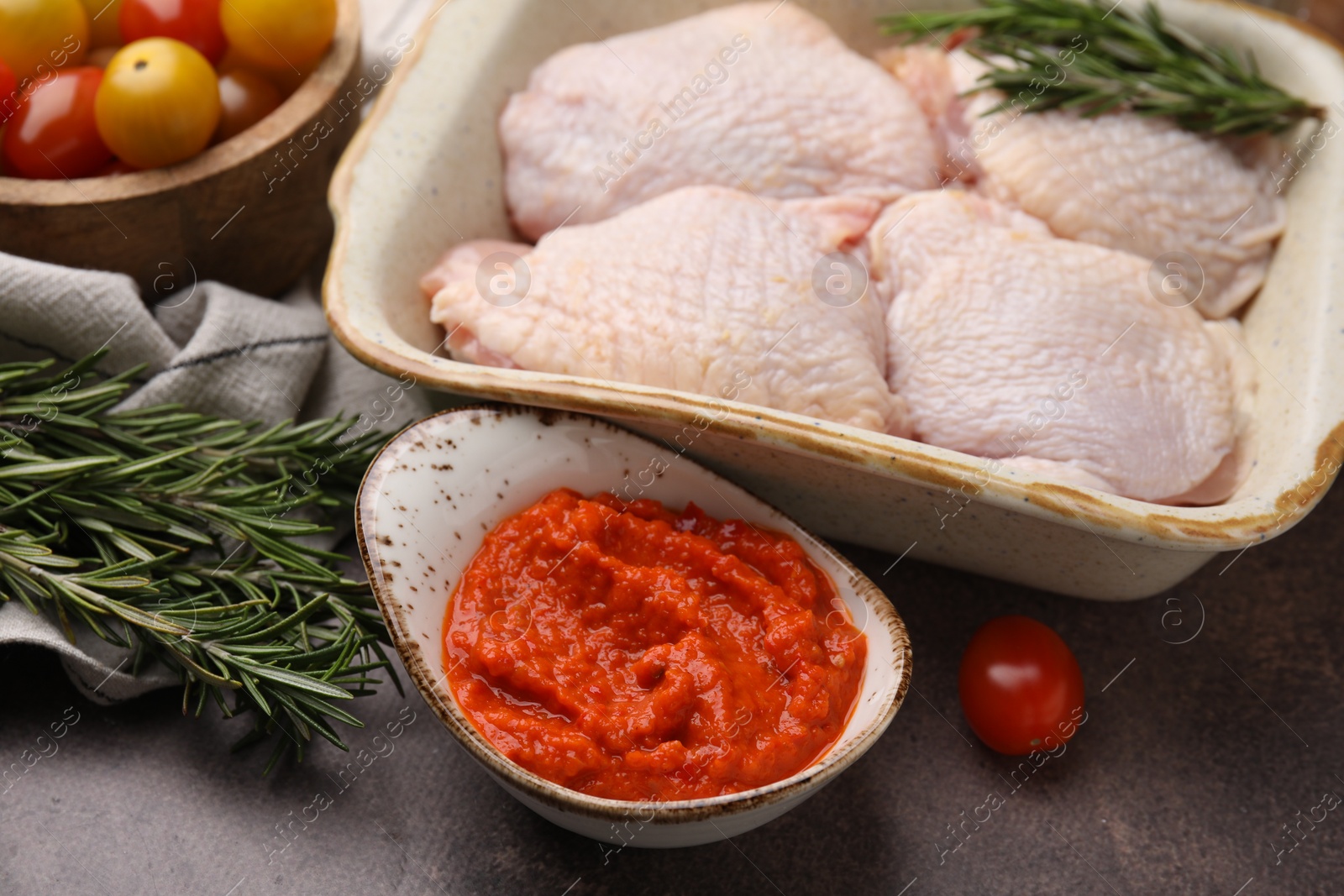 Photo of Marinade, raw chicken and rosemary on brown table, closeup