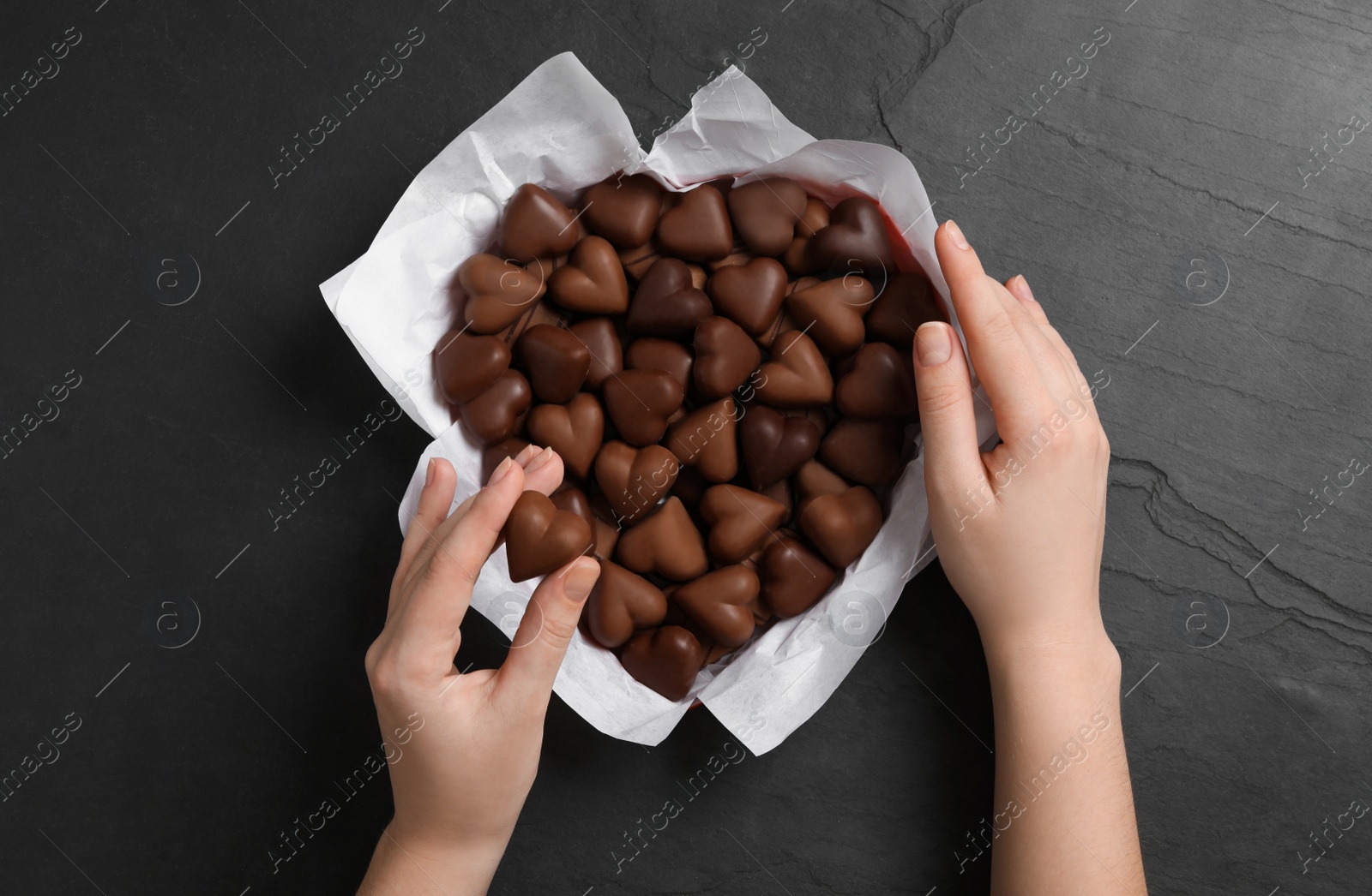 Photo of Woman with box of heart shaped chocolate candies at black table, top view