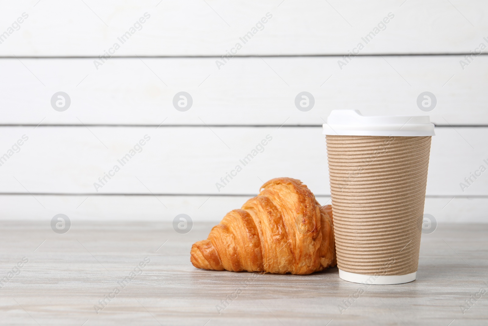 Photo of Coffee to go. Paper cup with tasty drink and croissant on white wooden table. Space for text