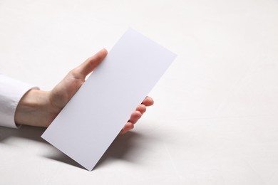 Woman holding blank card at white table, closeup. Mockup for design