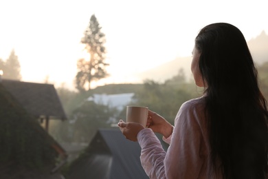 Photo of Young woman with cup of tea enjoying beautiful view in morning