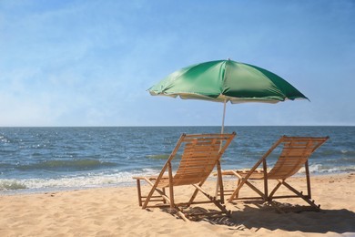 Photo of Green beach umbrella and deck chairs on sandy seashore