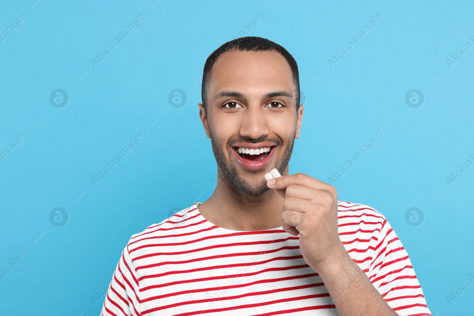 Photo of Portrait of happy young man with bubble gums on light blue background