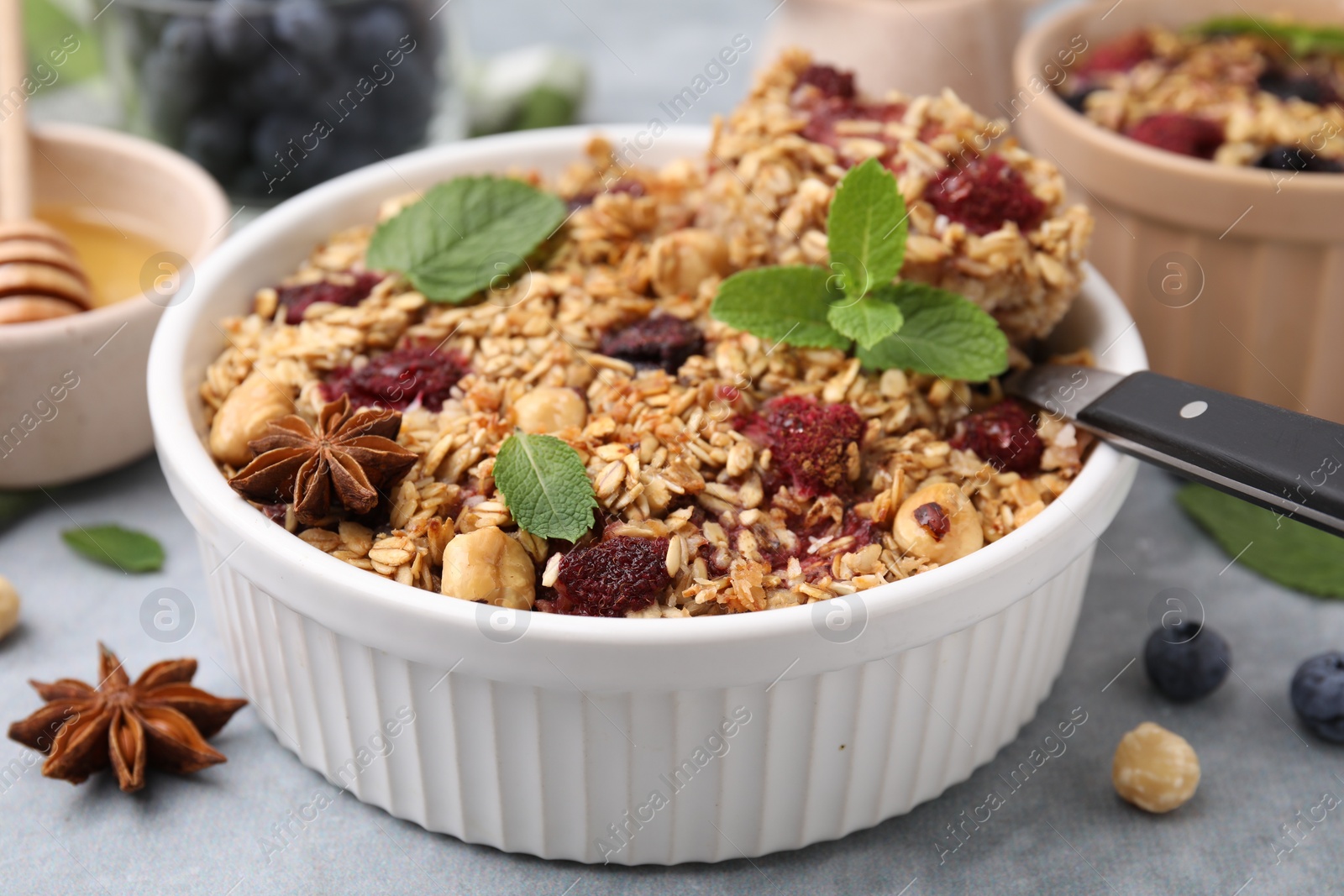 Photo of Tasty baked oatmeal with berries, nuts and anise star on light grey table, closeup