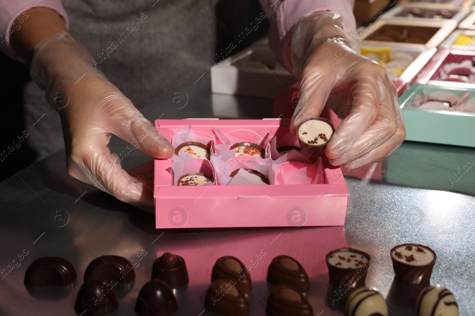 Photo of Woman packing delicious candies into pink box at production line, closeup