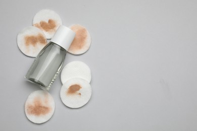 Bottle of makeup remover, clean and dirty cotton pads on light grey background, flat lay. Space for text