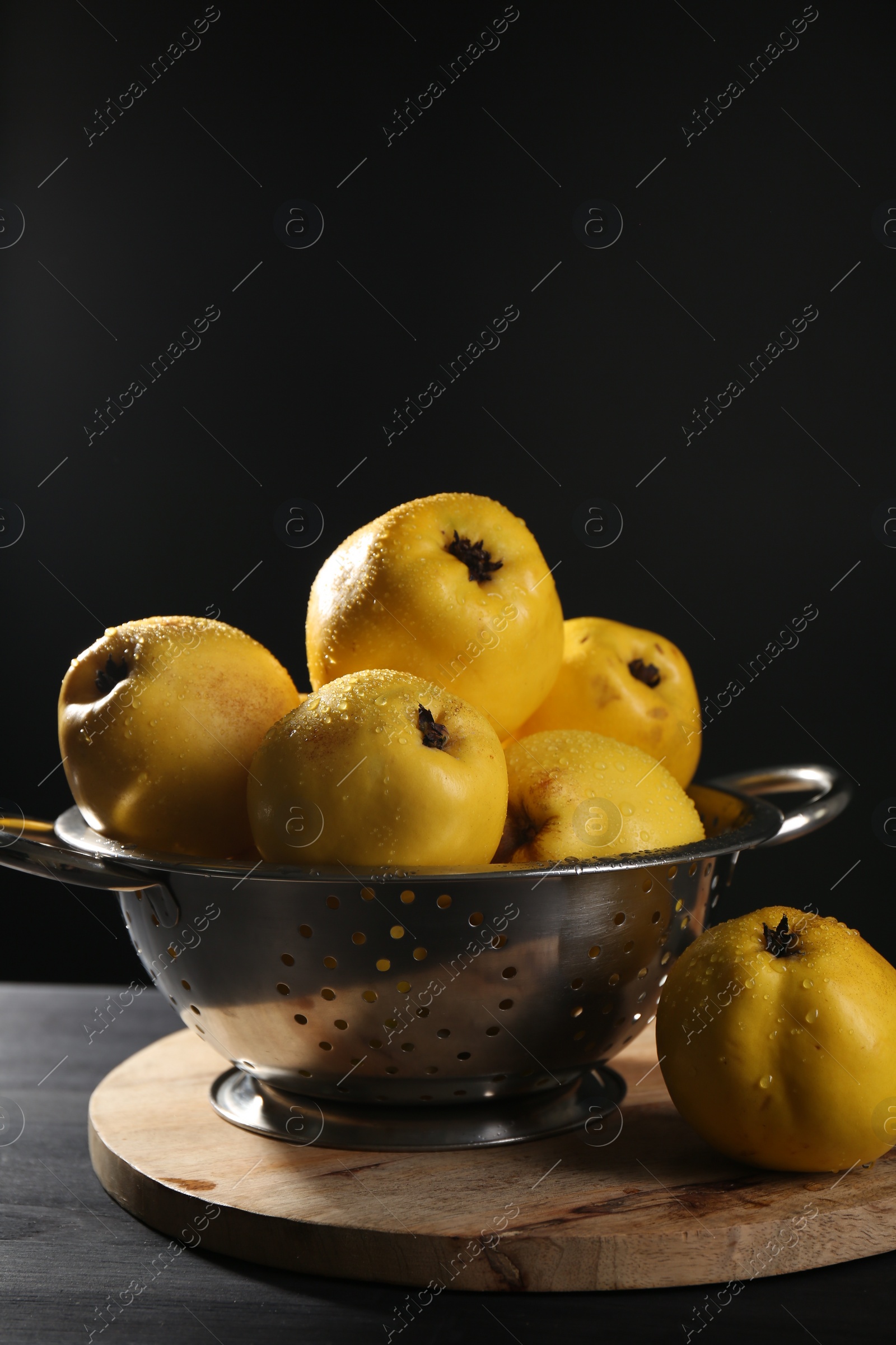 Photo of Tasty ripe quinces with water drops in metal colander on black wooden table