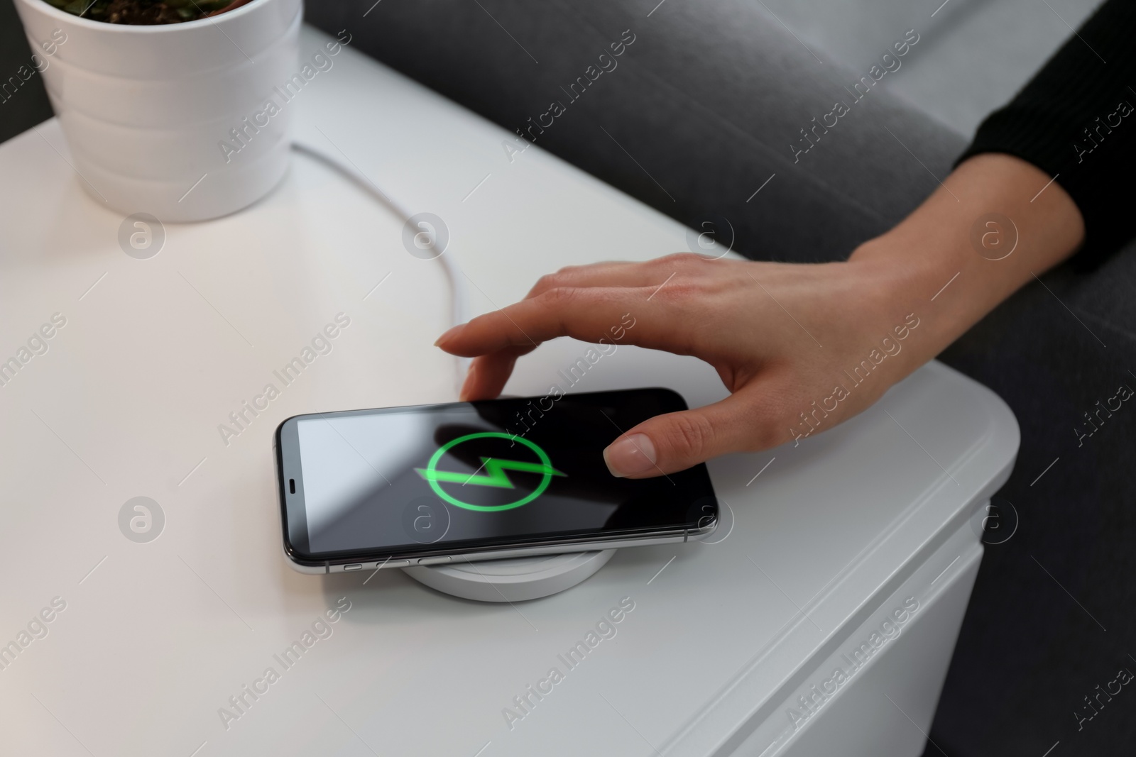 Photo of Woman taking smartphone from wireless charger in room, closeup
