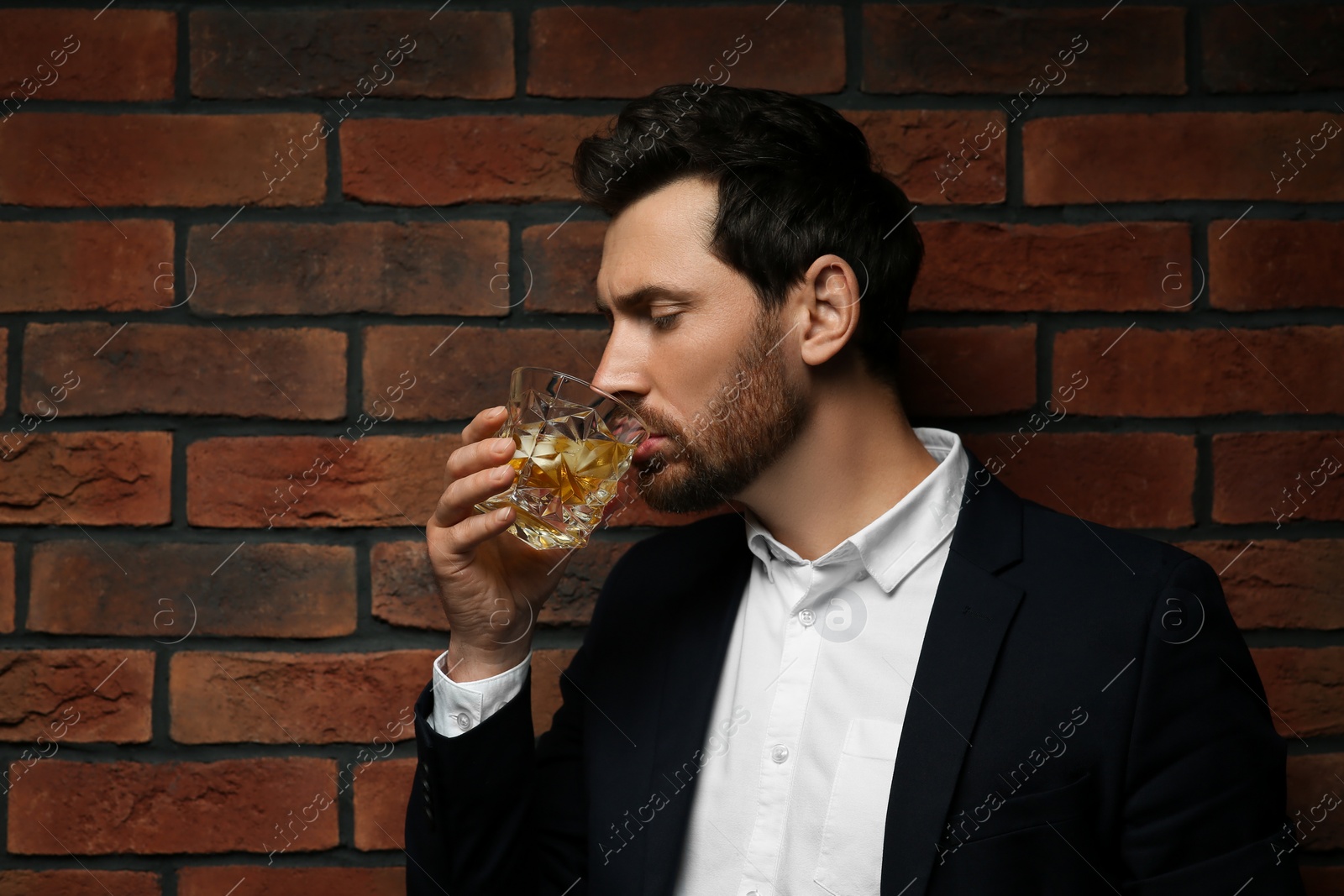 Photo of Man in suit drinking whiskey near red brick wall. Space for text