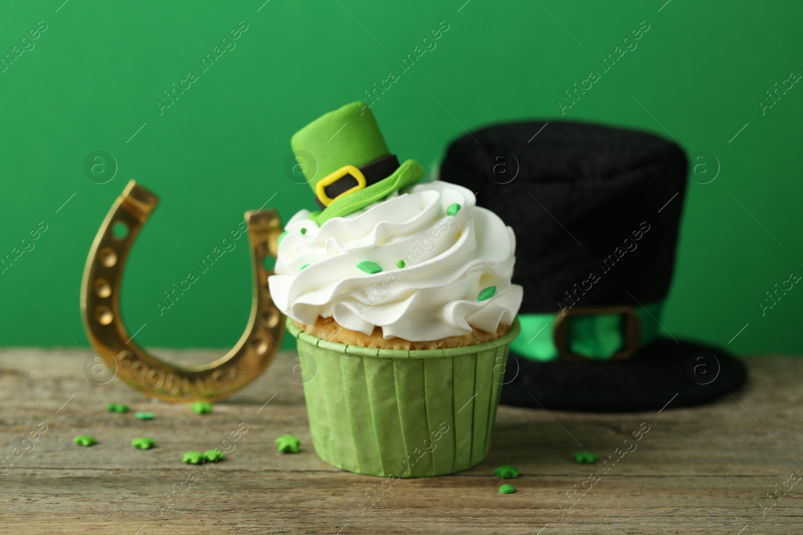 Photo of St. Patrick's day party. Tasty cupcake with leprechaun hat topper and gold horseshoe on wooden table