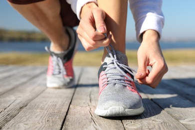 Sporty woman tying shoelaces outdoors on sunny morning, closeup