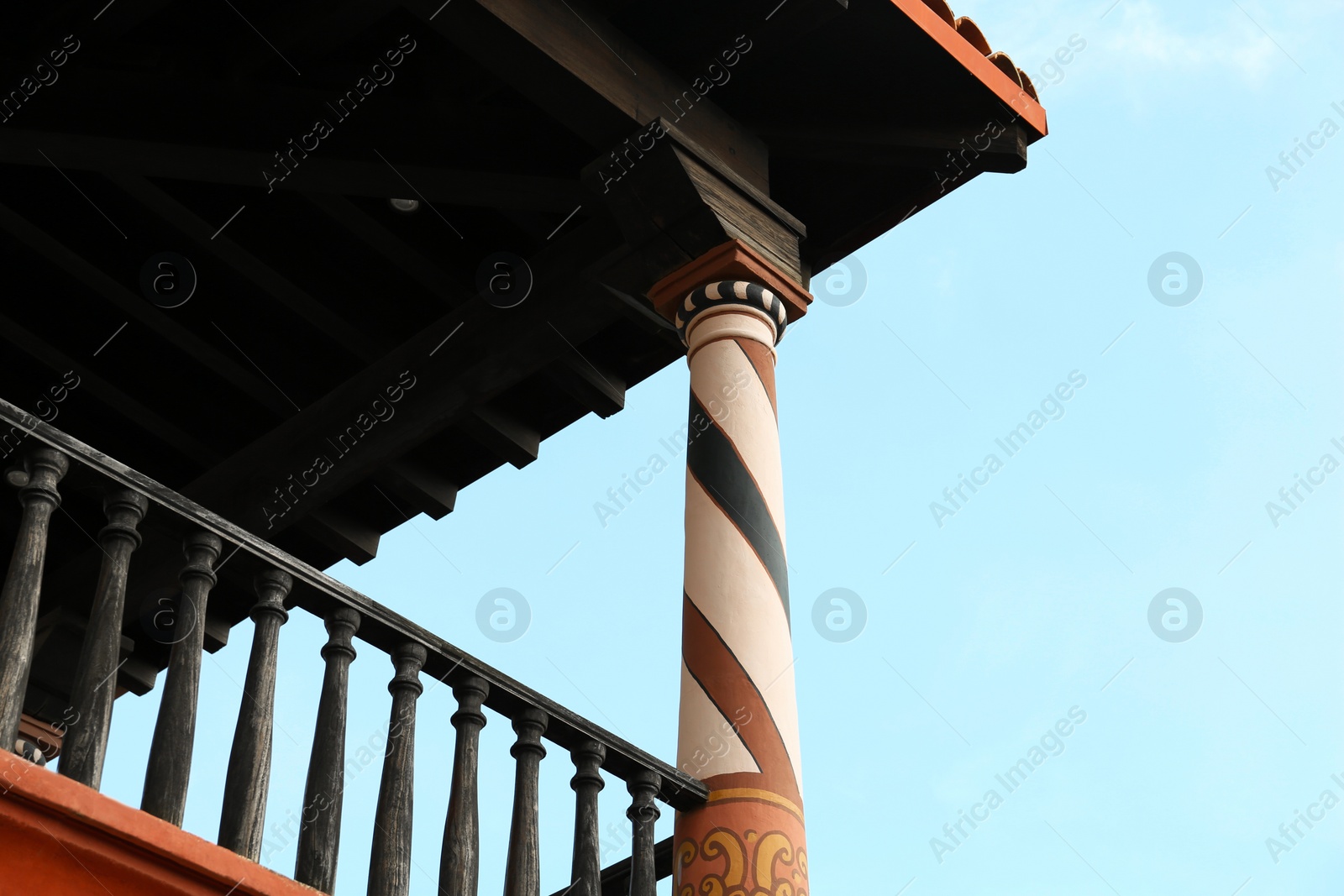 Photo of Exterior of beautiful building with wooden railing and roof against blue sky, low angle view. Space for text