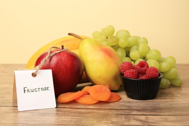 Card with word Fructose, delicious ripe fruits, raspberries and dried apricots on wooden table