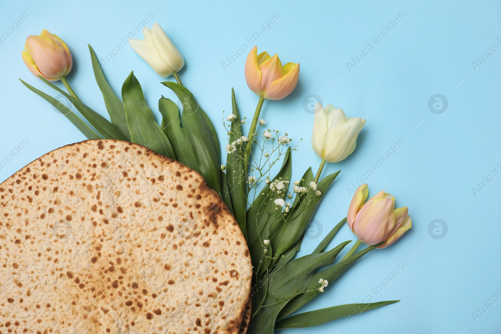 Photo of Tasty matzos and fresh flowers on light blue background, flat lay. Passover (Pesach) celebration