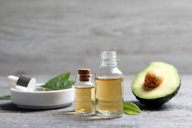 Photo of Bottles of essential oil and fresh avocado on grey wooden table