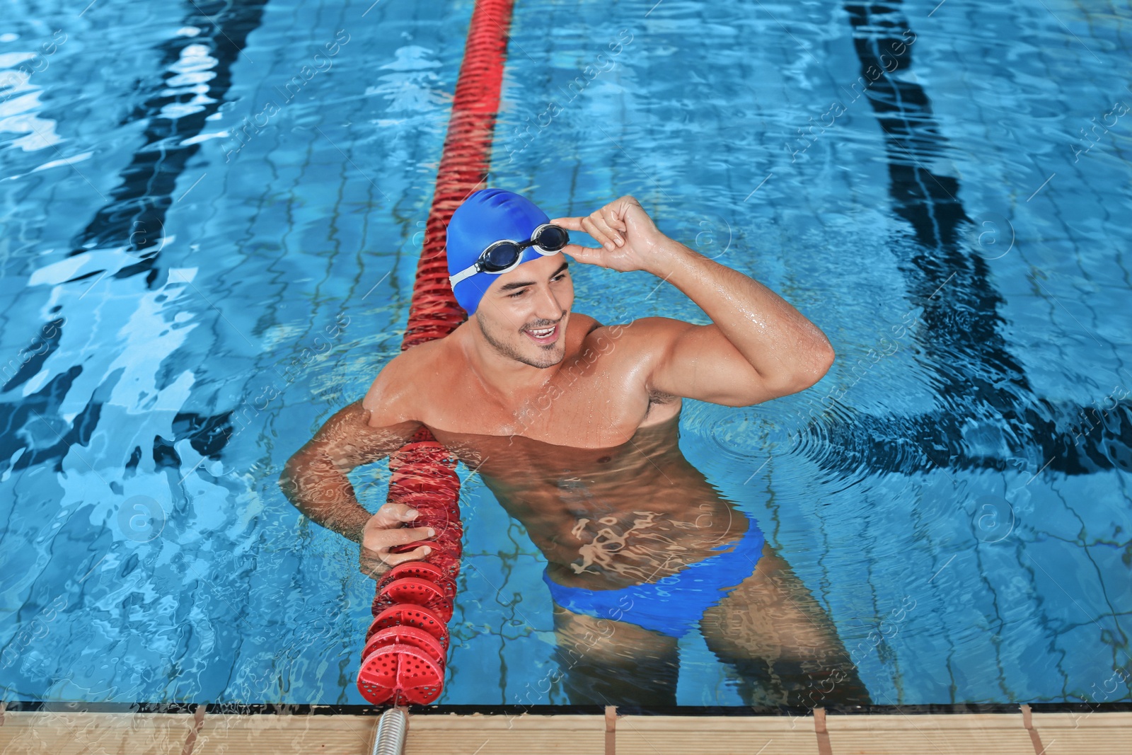 Photo of Young athletic man wearing cap and goggles in swimming pool