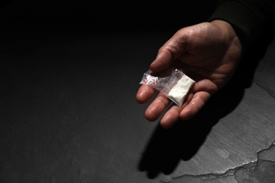 Addicted man with plastic bag of hard drug at grey textured table, closeup. Space for text