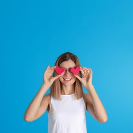 Portrait of woman holding decorative hearts near eyes on color background