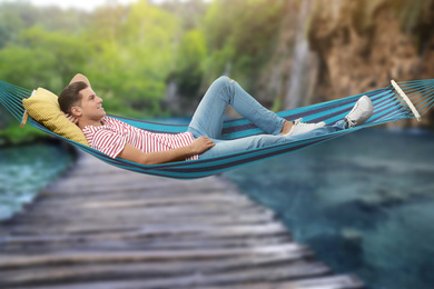 Man resting in hammock near waterfall on sunny day 