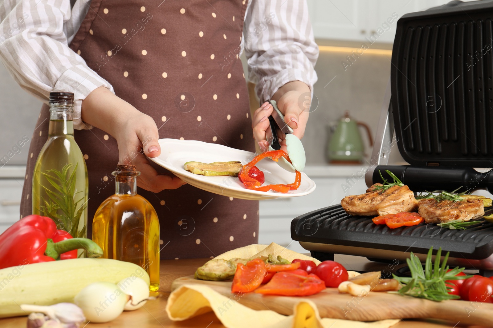 Photo of Woman cooking different products with electric grill at wooden table in kitchen, closeup