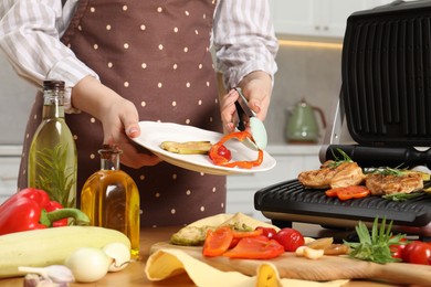 Woman cooking different products with electric grill at wooden table in kitchen, closeup