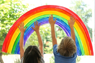 Photo of Children touching picture of rainbow on window. Stay at home concept