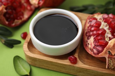 Photo of Tasty pomegranate sauce in bowl and fruits on green table, closeup