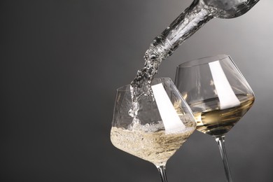 Photo of Pouring white wine into glass against grey background, closeup. Space for text