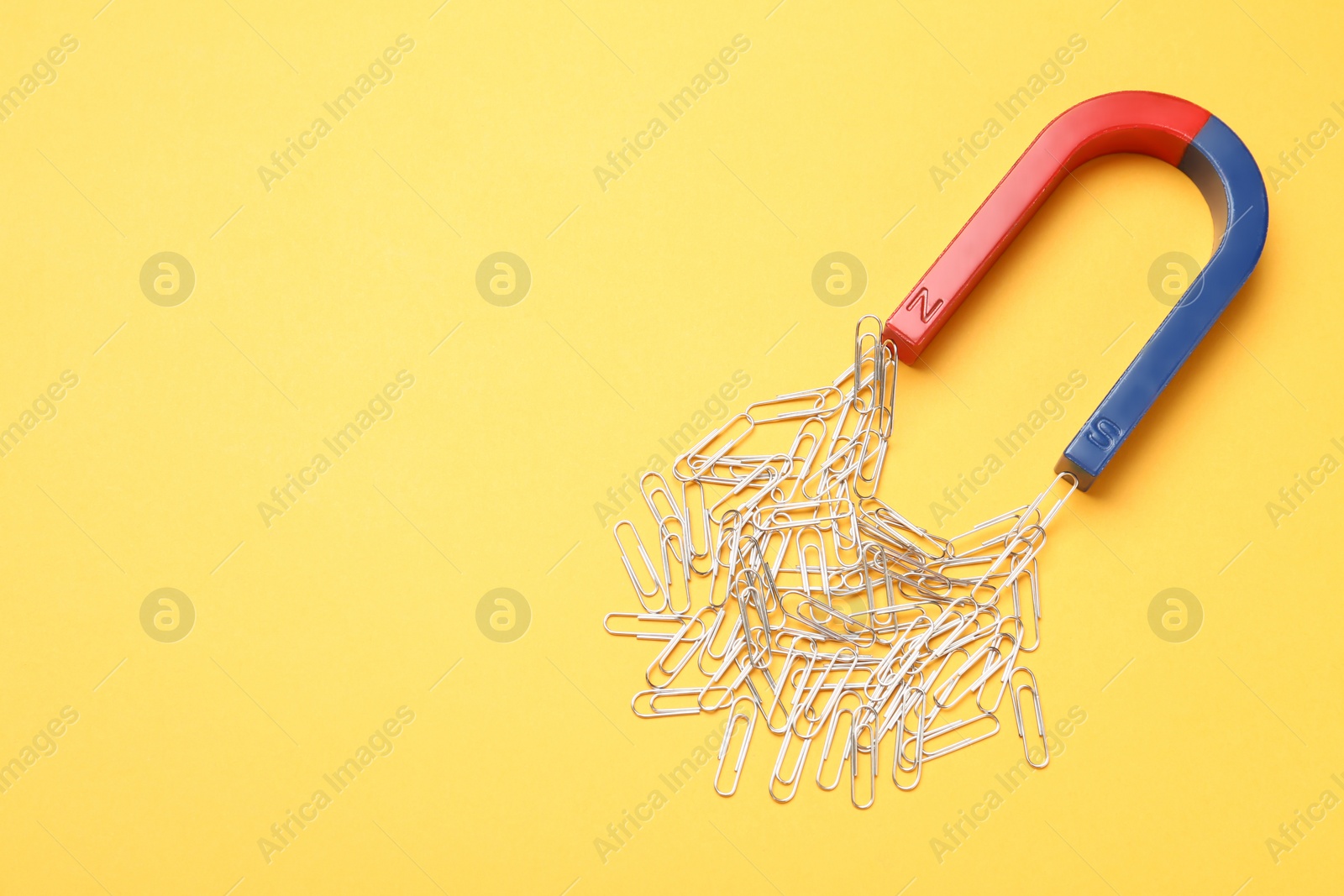 Photo of Magnet attracting paper clips on color background, top view with space for text