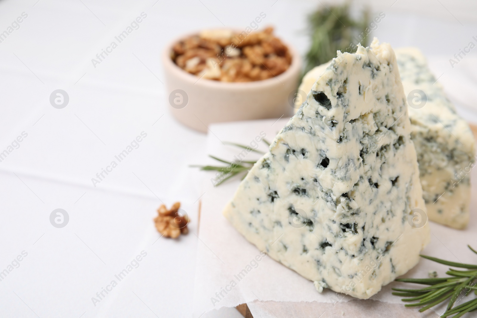 Photo of Tasty blue cheese with rosemary and walnuts on white tiled table, closeup. Space for text