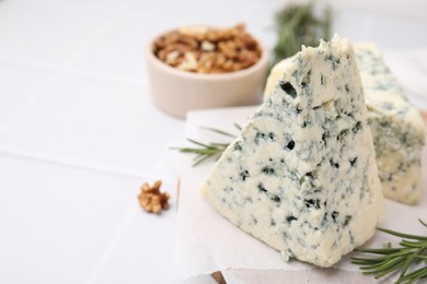 Photo of Tasty blue cheese with rosemary and walnuts on white tiled table, closeup. Space for text