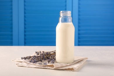 Bottle of tasty milk and lavender flowers on table against light blue wall, space for text