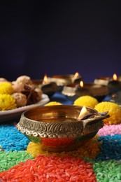 Diwali celebration. Diya lamps and colorful rangoli on table against violet background, closeup. Space for text