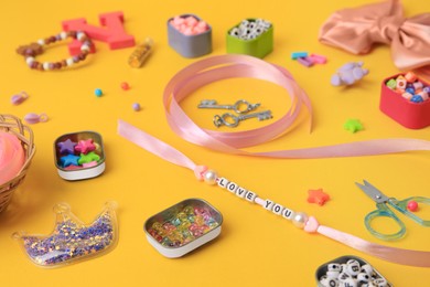Photo of Handmade jewelry kit for kids. Colorful beads, ribbon and different supplies on orange background, closeup
