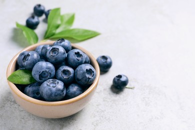 Photo of Tasty fresh blueberries in bowl on light grey table, space for text