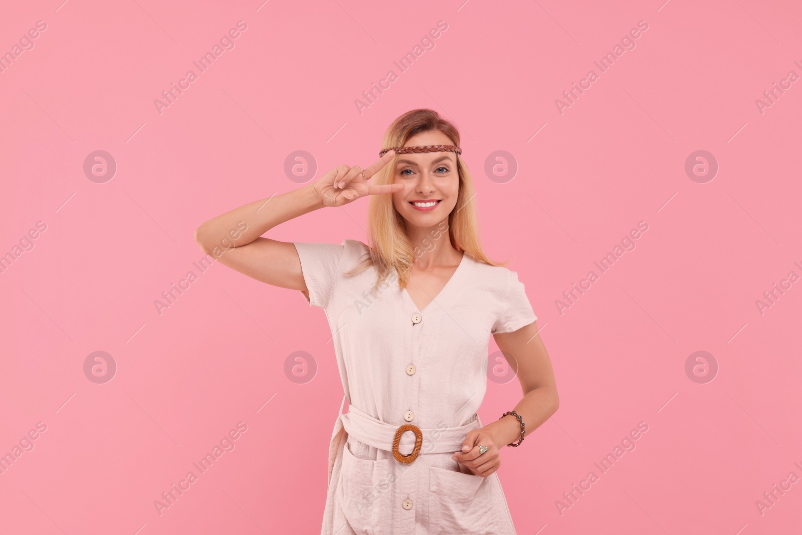 Photo of Portrait of smiling hippie woman showing peace sign on pink background